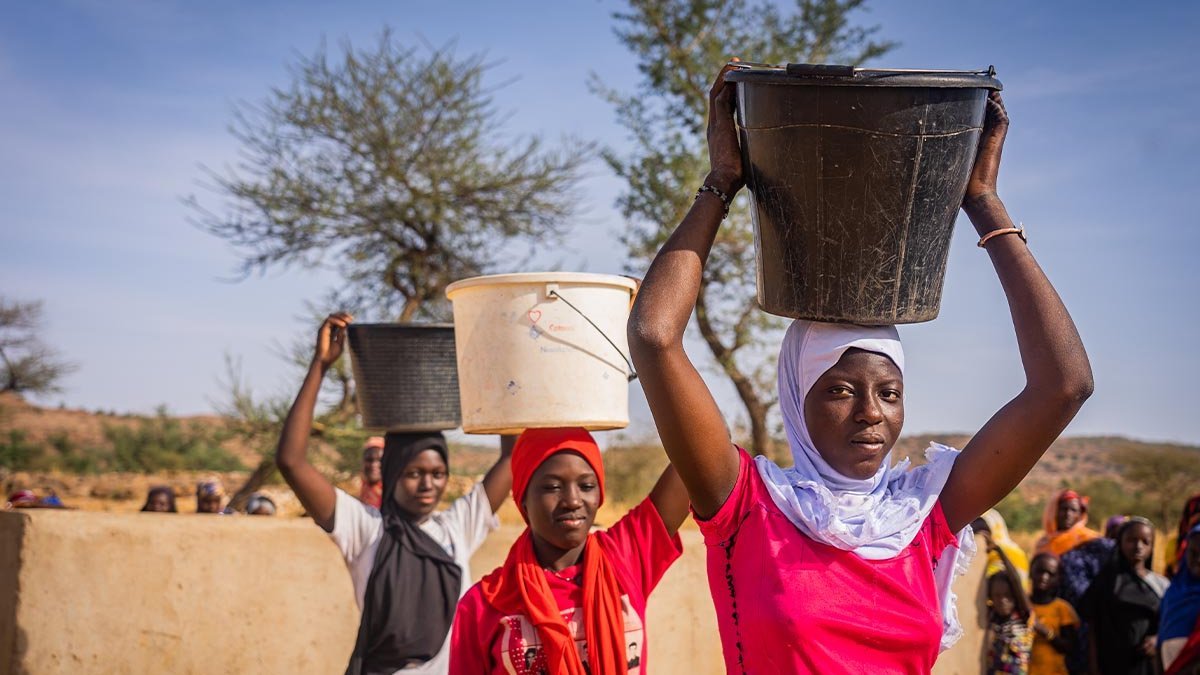 Spenden Mali: Sauberes Wasser dank Brunnen von Help Drei malische junge Frauen tragen Wasser-Eimer auf dem Kopf