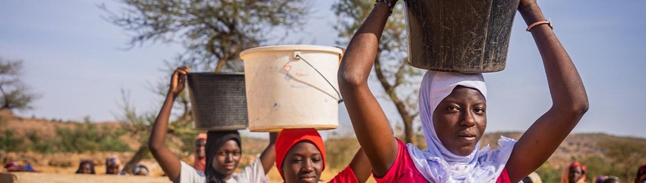 Drei malische junge Frauen tragen Wasser-Eimer auf dem Kopf