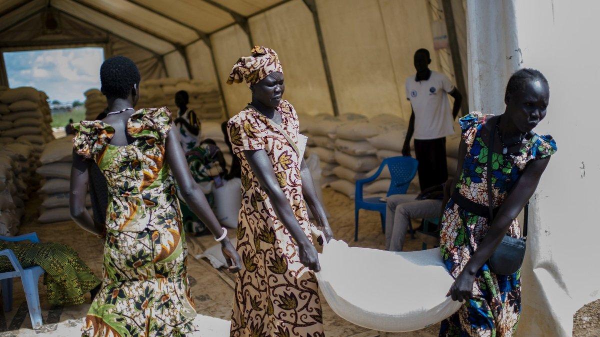 Nahrungsmittelhilfe in Mingkaman, Südsudan Zwei südsudanesische Frauen tragen gemeinsam einen Sack mit Nahrungsmitteln