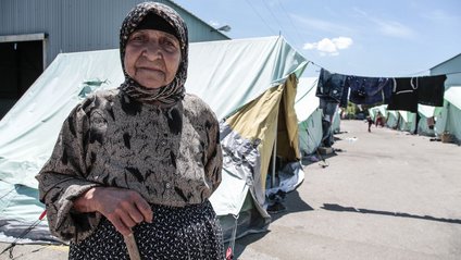 Alte Frau vor einem Zeltlager in Griechenland