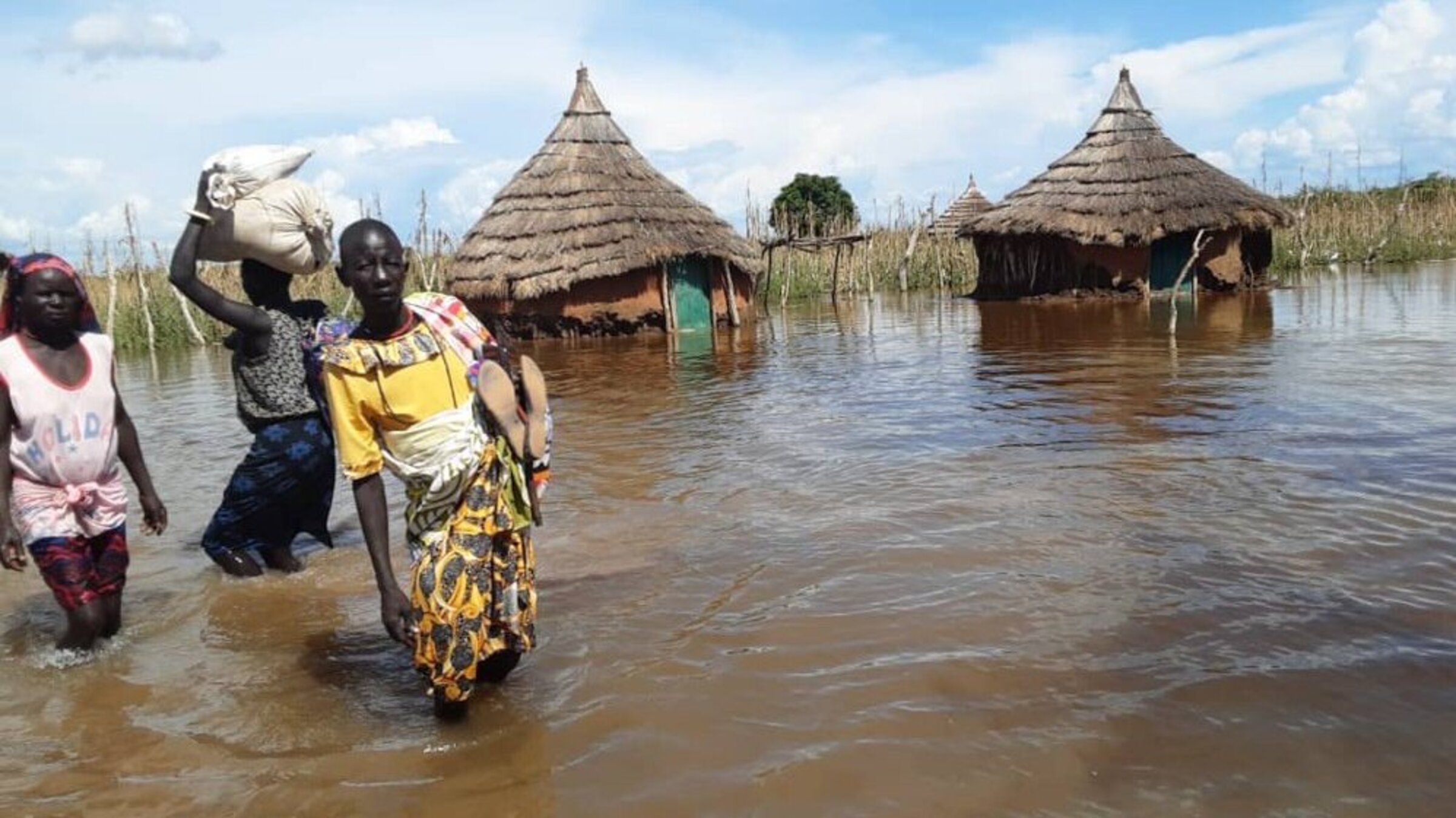 Three South Sudanese women stand in knee-high water