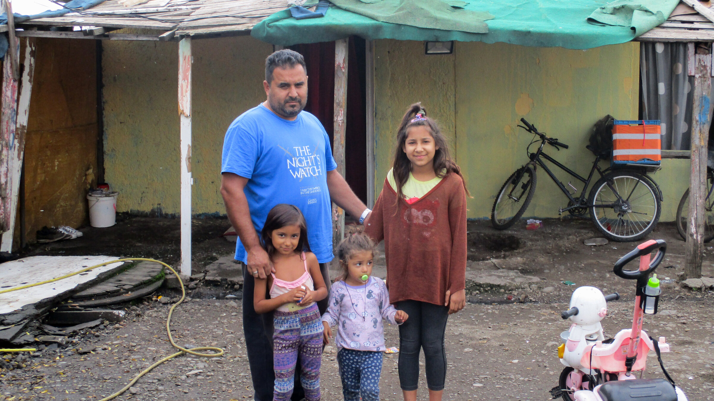 A man stands with three children in front of a badly damaged house with a makeshift repaired roof