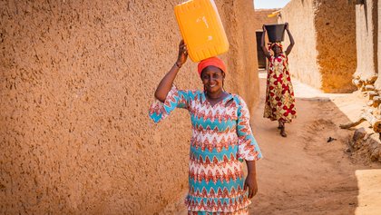 Frau aus Mali trägt Wasserkanister