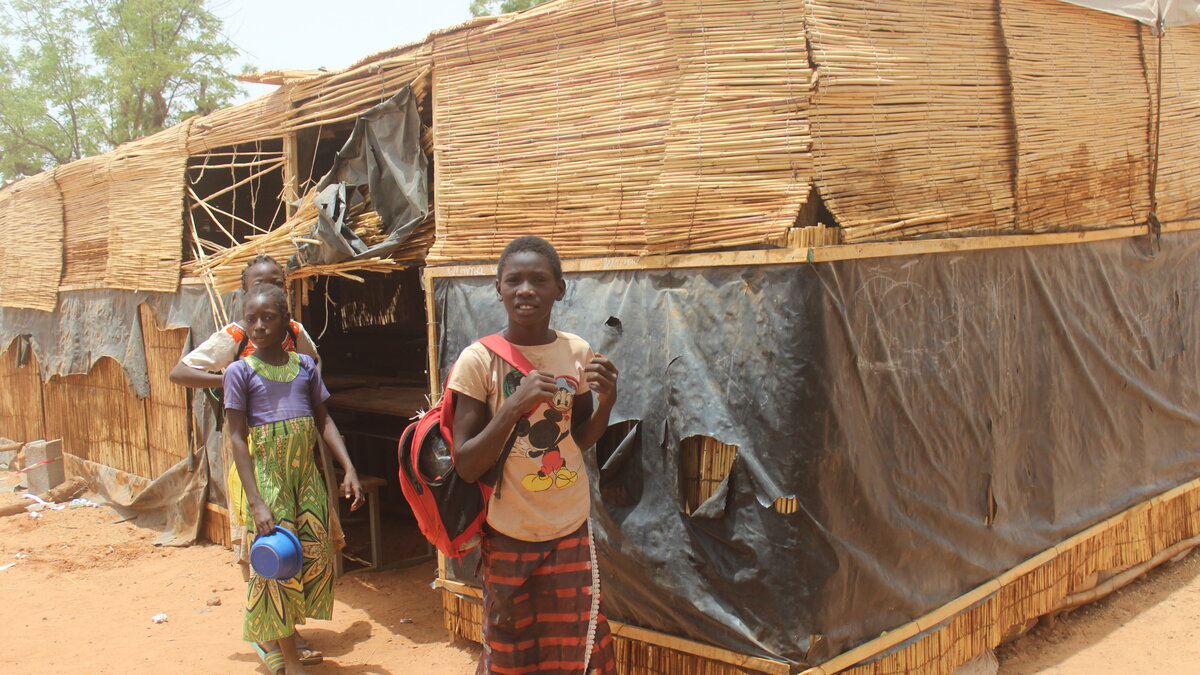 Drei Mädchen stehen vor einer Strohhüttenschule in Burkina Faso