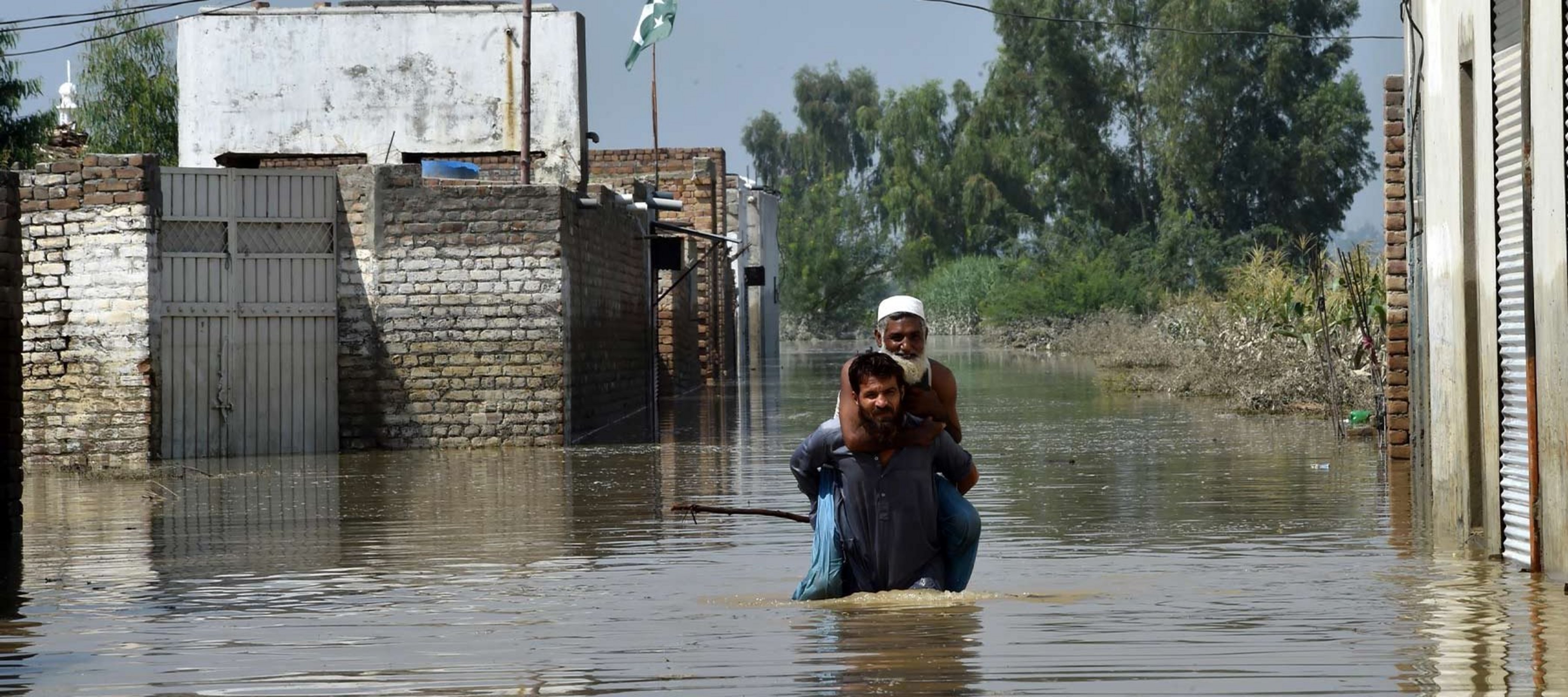 Zwei Männer waten durch Hochwasser in Pakistan
