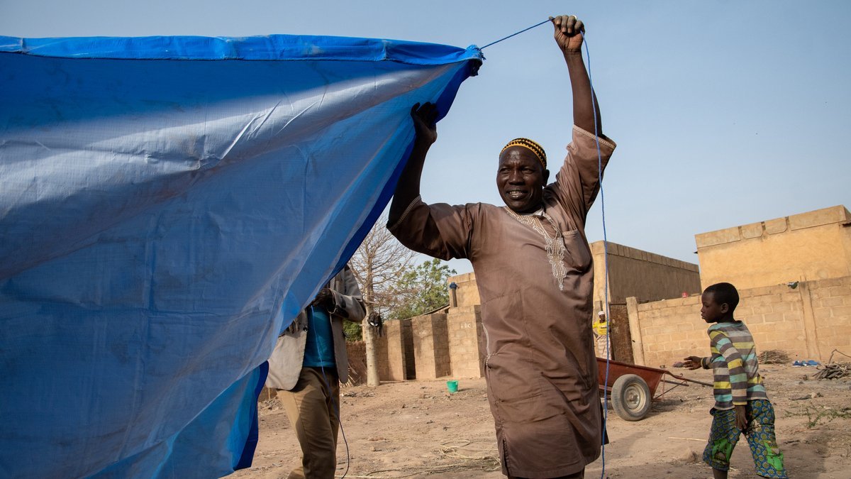 Ein geflüchteter Mann aus Burkina Faso beim Aufbau eines Zeltes, das als Notunterkunft dient