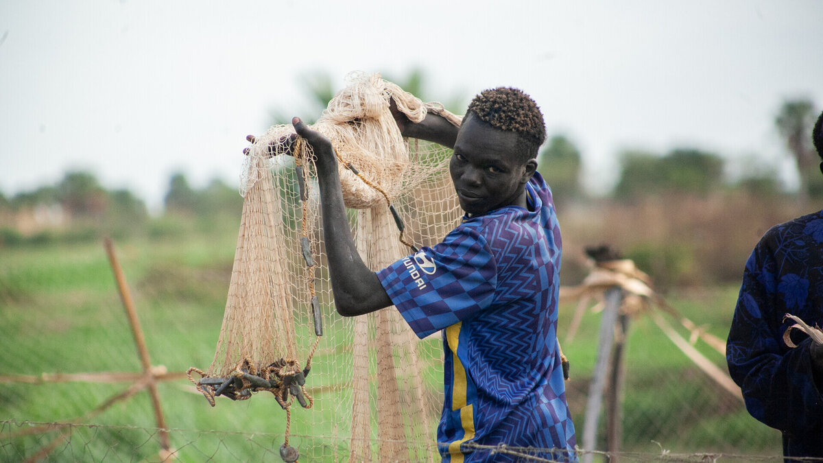  A young South Sudanese man holds a fishing net and looks into the camera