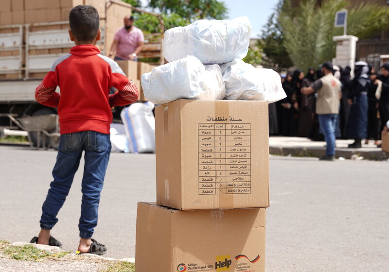 Ein syrischer Junge steht neben Hilfspaketen