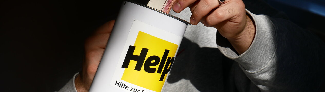 Eine Hand steckt einen 10-Euro-Schein in eine Spendendose