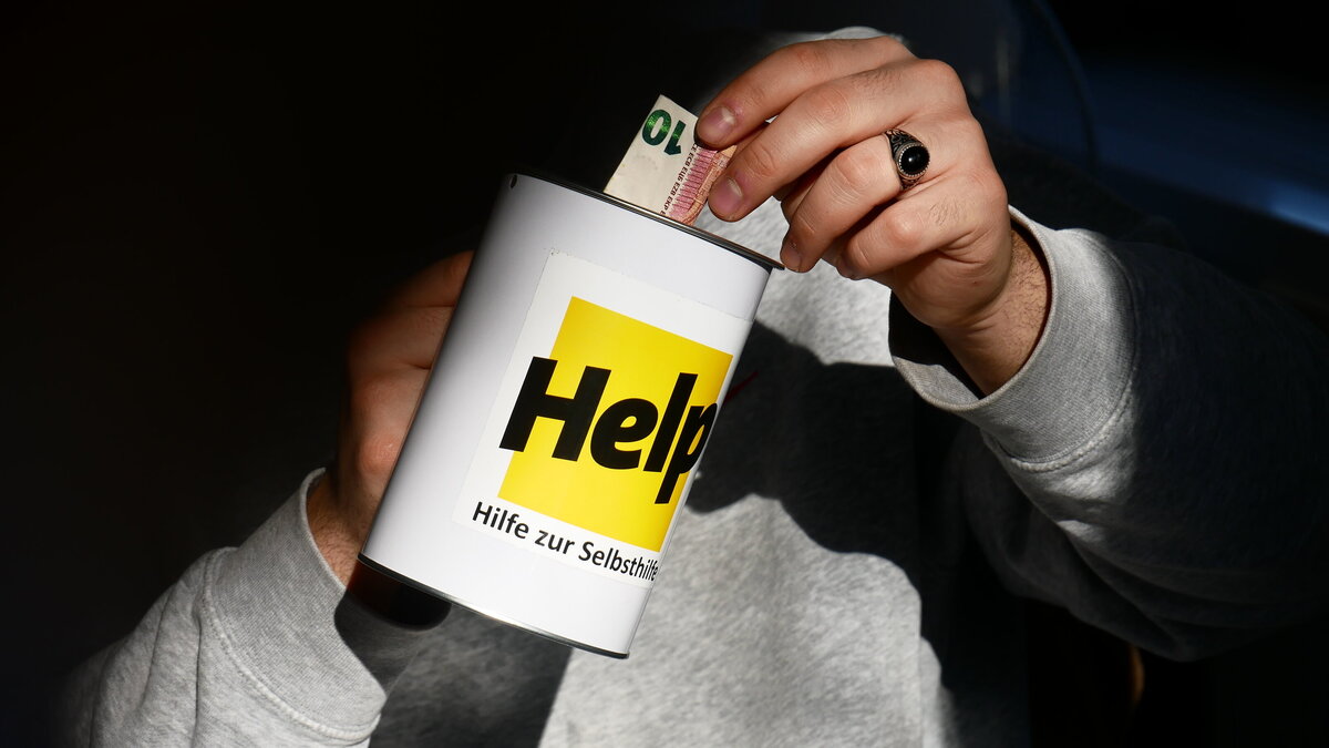 Eine Hand steckt einen 10-Euro-Schein in eine Spendendose