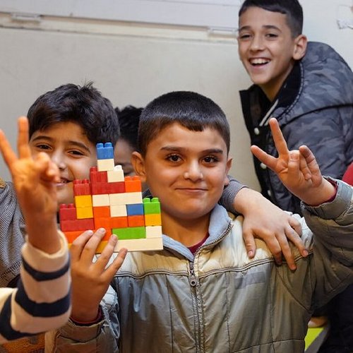 Kinder halten lachend ihr Spielzeug und Peace-Handzeichen in die Kamera