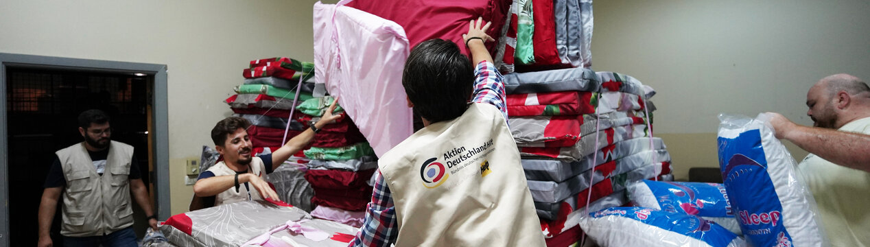 Drei humanitäre Helfer stehen vor Matratzen und Kissen