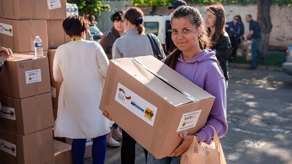 Eine junge Frau hält ein Hilfspaket von Help und lächelt