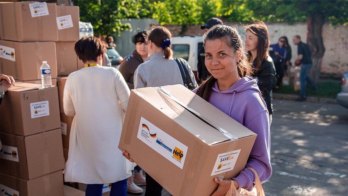 Eine junge Frau hält ein Hilfspaket von Help und lächelt