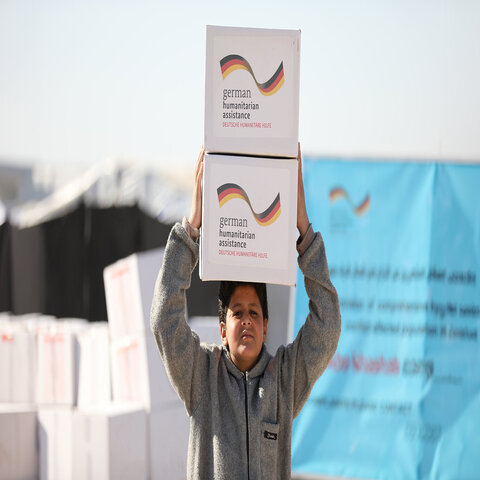 Ein syrischer Junge trägt zwei Hilfspakete mit der Aufschrift "German Humanitarian Assistance" auf seinem Kopf