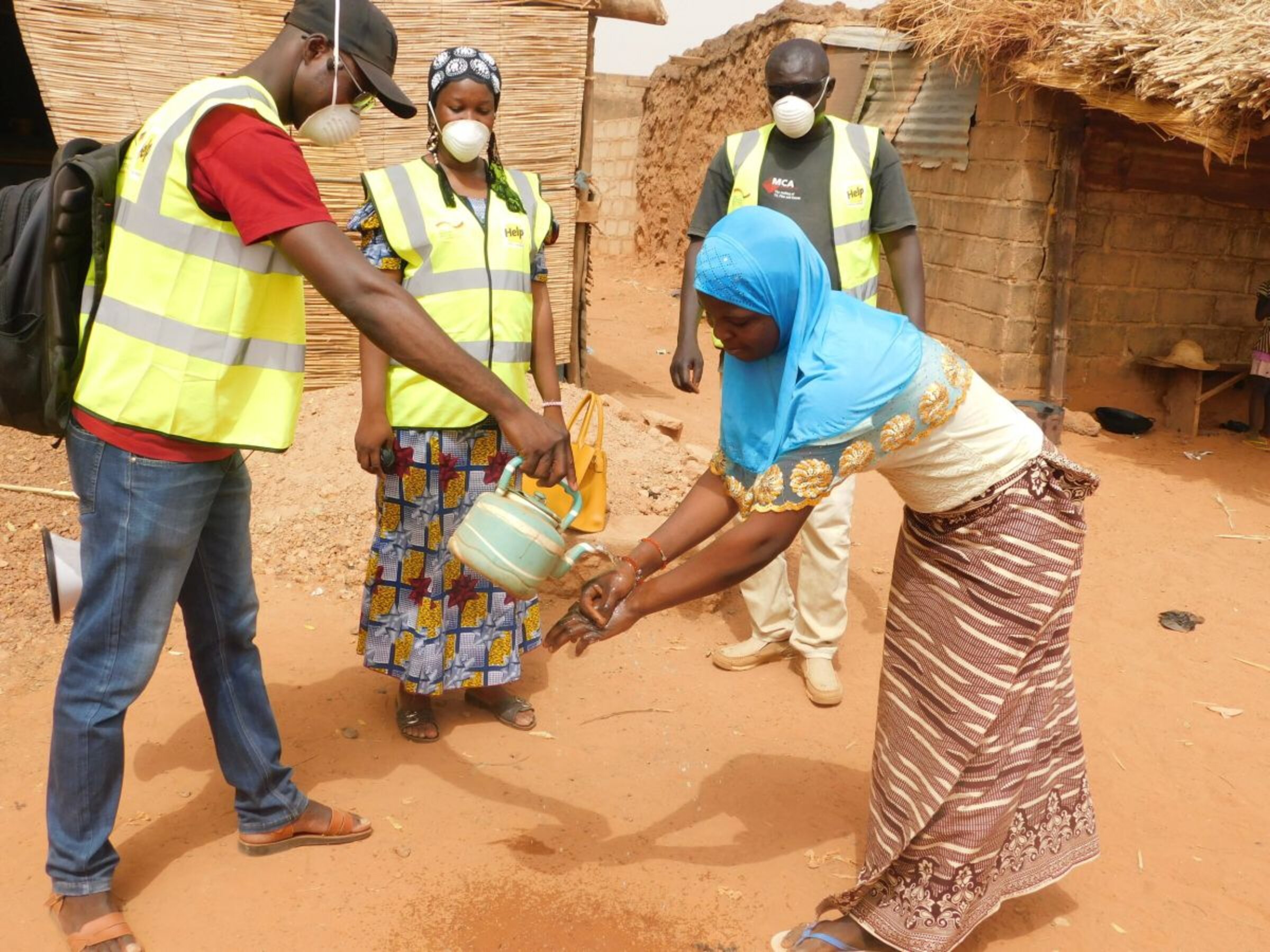 Ein Help-Mitarbeiter erklärt einer Frau in Burkina Faso, wie man sich die Hände wäscht, um sich nicht mit Corona zu infizieren.