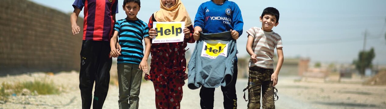 Springende Kinder im Irak mit Help Logos in den Händen
