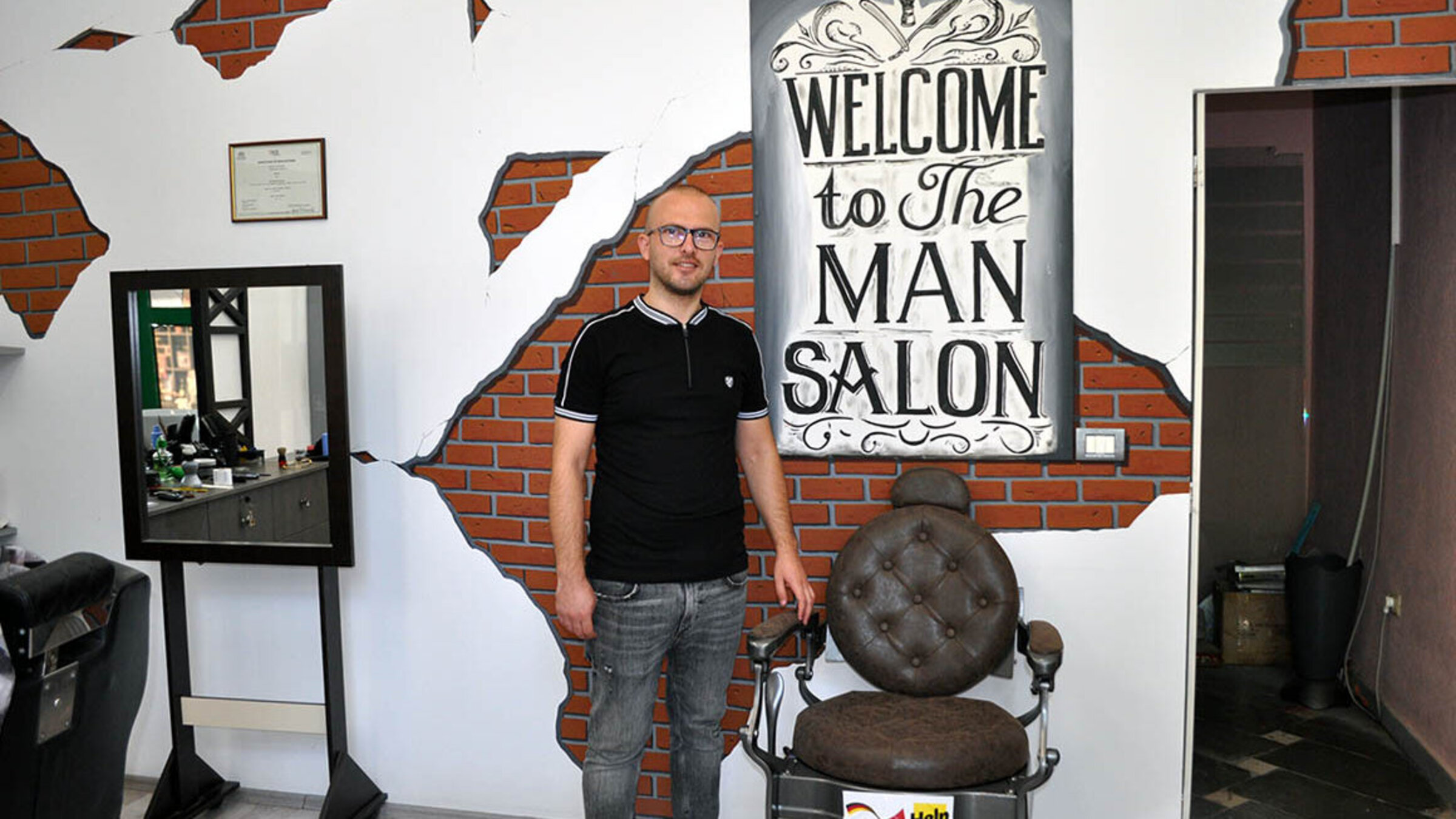Friseur Skerdi steht in seinem Salon, den er dank Help eröffnen konnte.