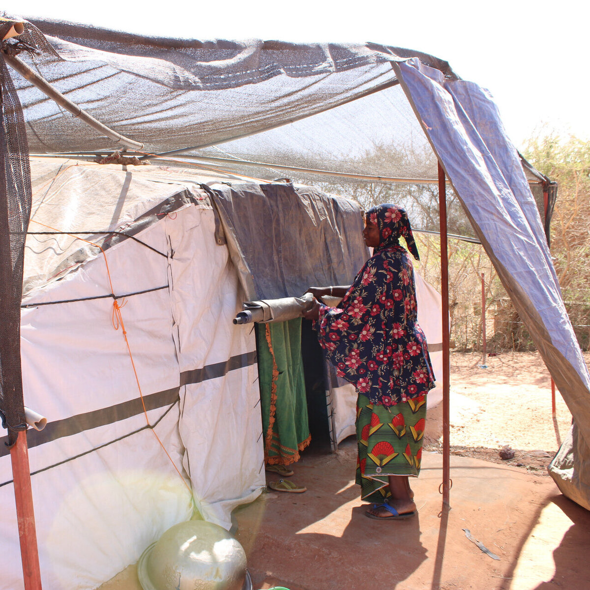 A Burkinabe woman stands in front of a tent for displaced families