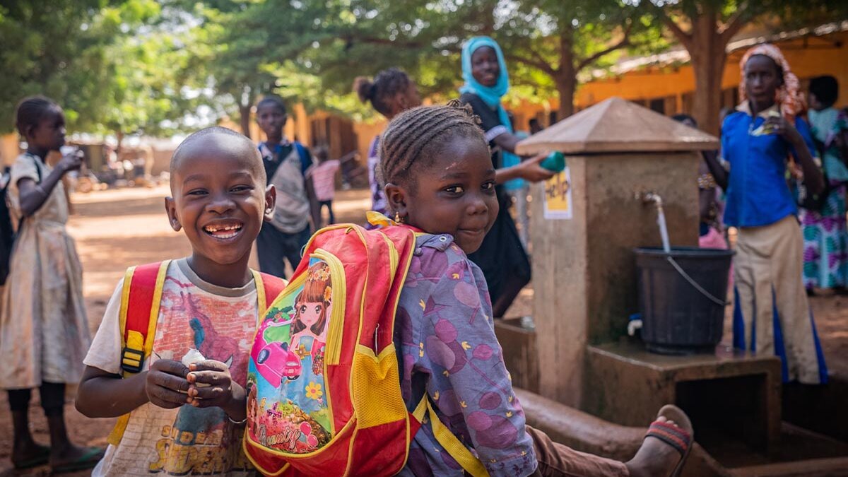 Zwei Schulkinder aus Mali sitzen vor einem Brunnen