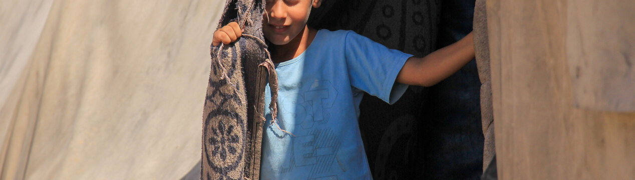 Ein syrischer Junge steht in einem Zelt und blickt schüchtern hervor