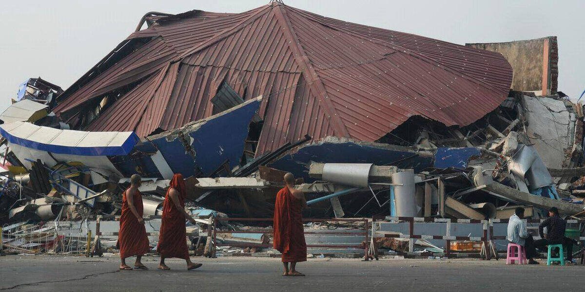 Drei Mönche stehen vor einem zerstörten Gebäude in Myanmar