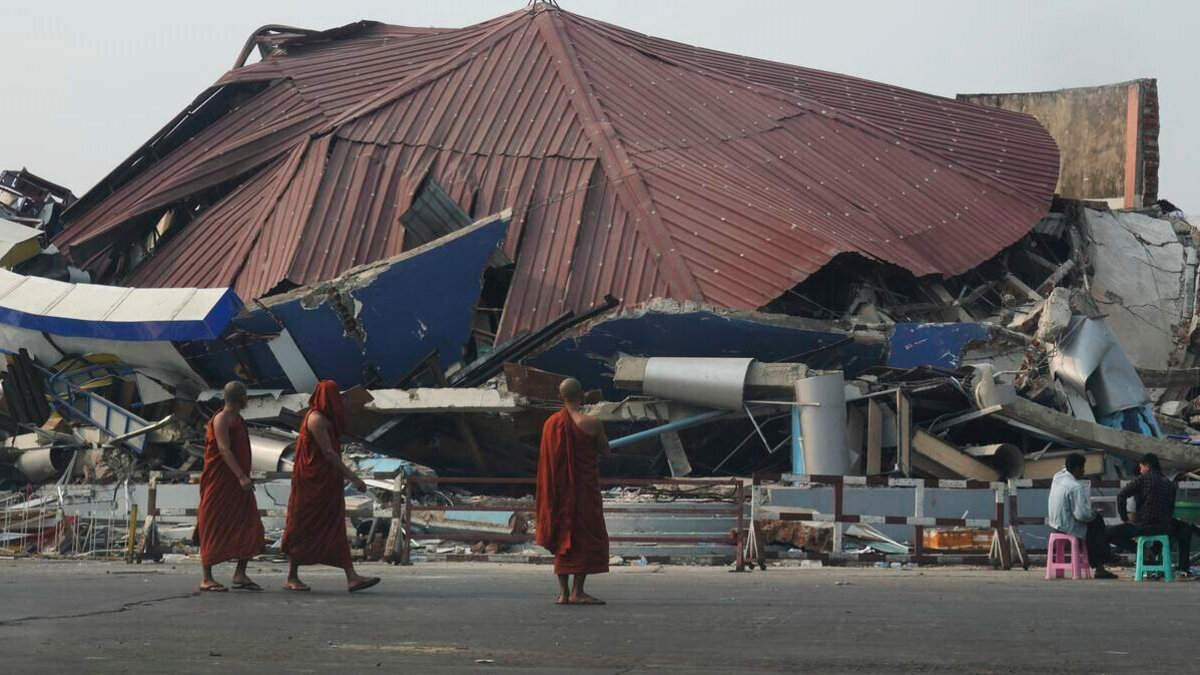 Drei Mönche stehen vor einem zerstörten Gebäude in Myanmar