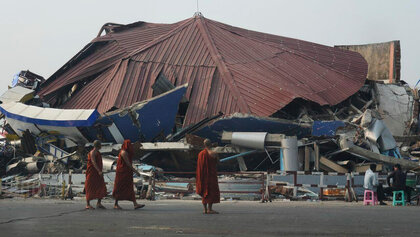 Drei Mönche stehen vor einem zerstörten Gebäude in Myanmar