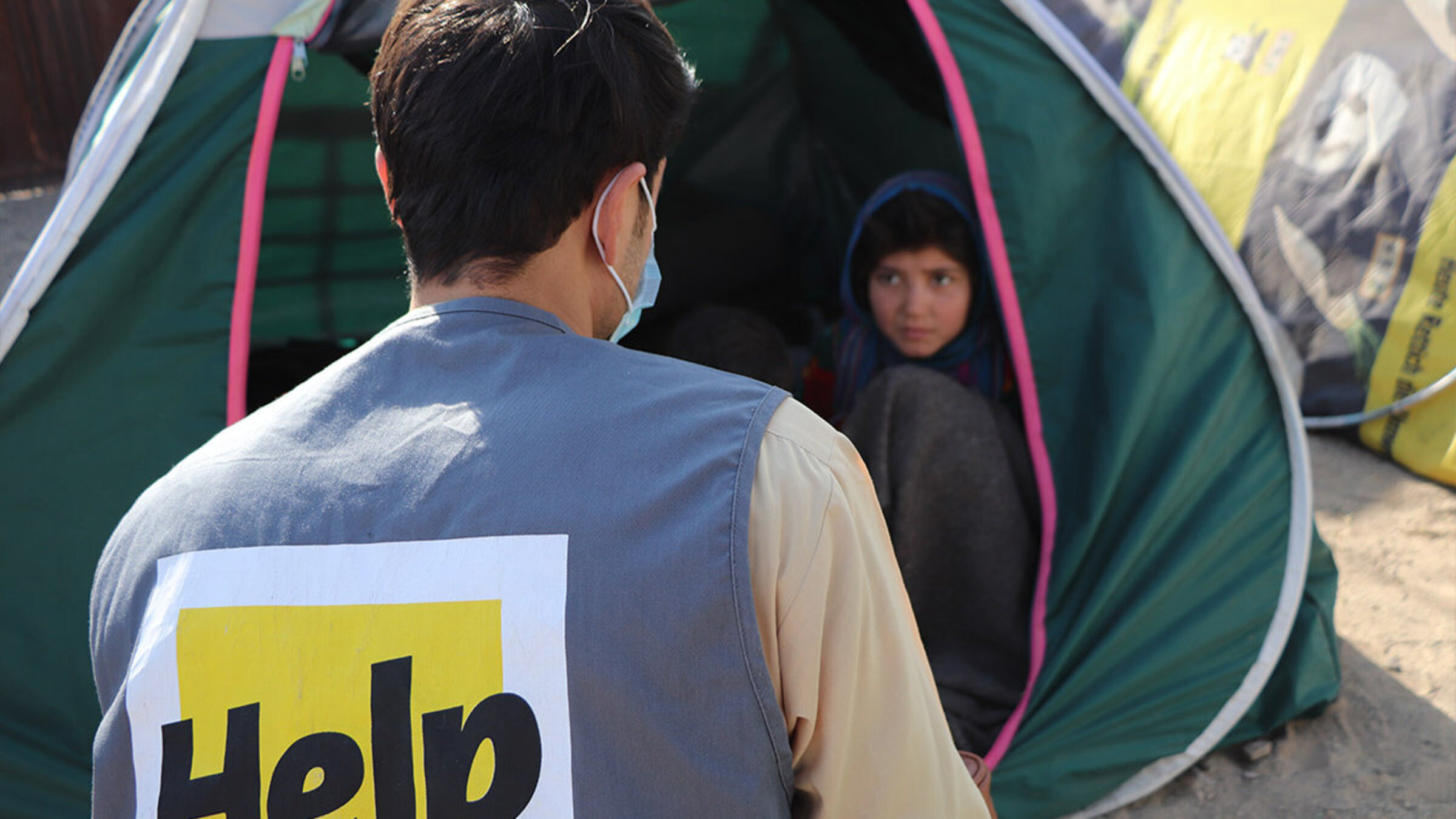 Ein Help-Mitarbeiter sitzt vor dem Zelt einer afghanischen Flüchtlingsfamilie
