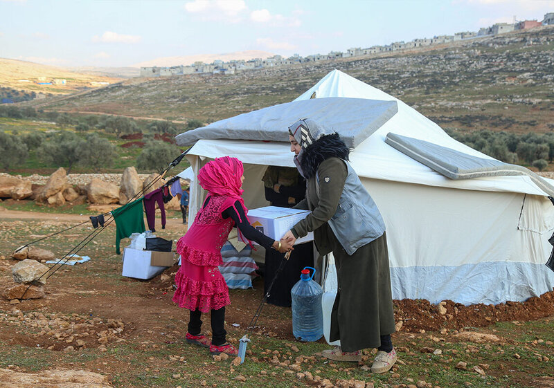 Eine Helferin überreicht einem syrischen Mädchen Hilfsgüter