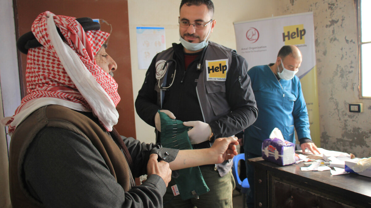 Medizinische Fachkraft bereitet die Blutdruckmessung bei einem syrischen Mann vor