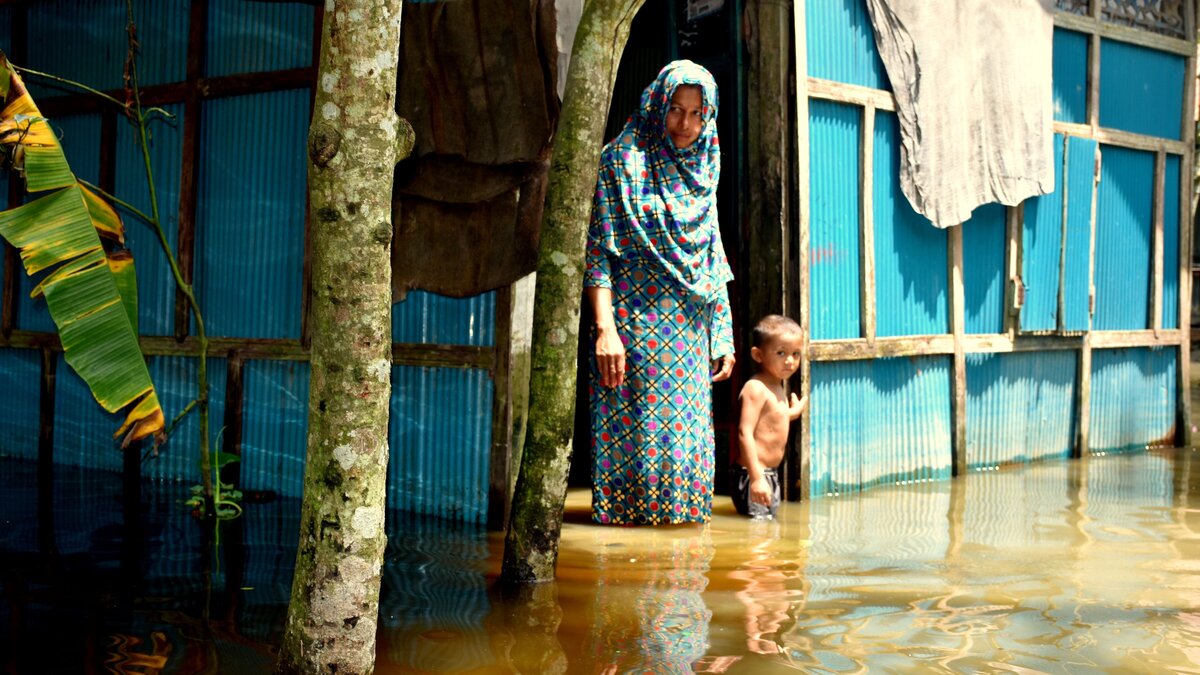 Eine Frau und ein Kind stehen in den Wassermassen, die ihr Haus umgeben