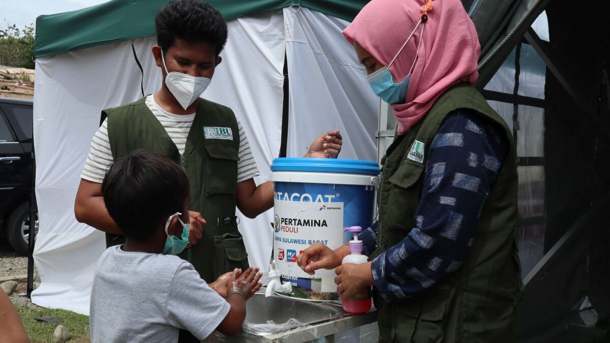 Zwei Mitarbeiter der Partnerorganisation vermitteln einem Kind gründliche Handhygiene