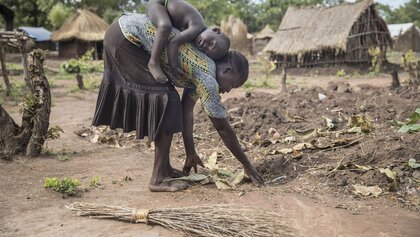 Südsudanesische Mutter bei der Ernte mit Kind auf dem Rücken