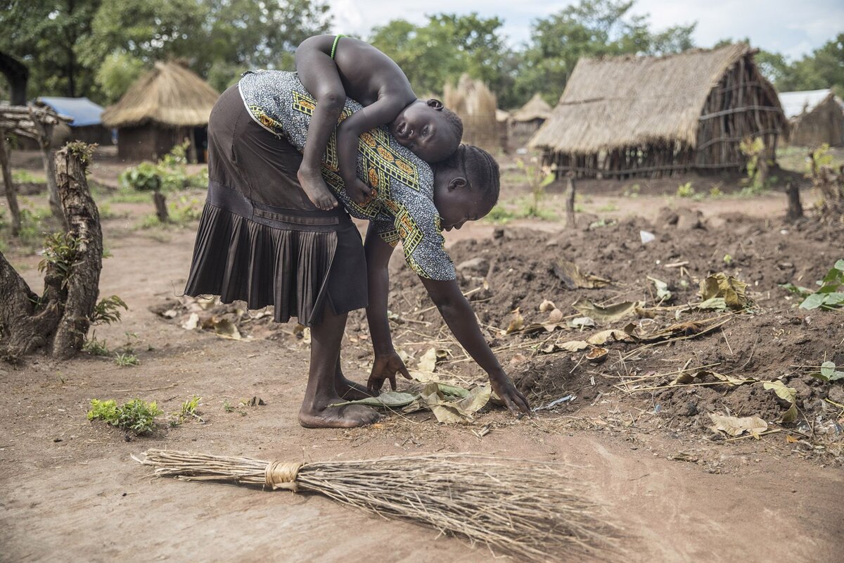 Südsudanesische Mutter bei der Ernte mit Kind auf dem Rücken
