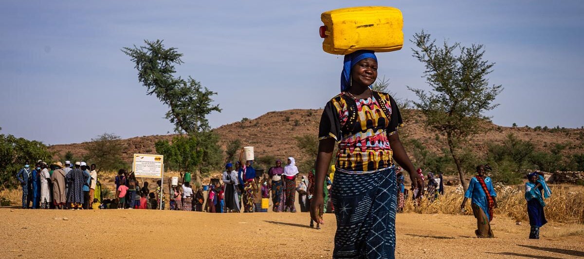 Eine Frau trägt einen gelben Wasserkanister auf dem Kopf