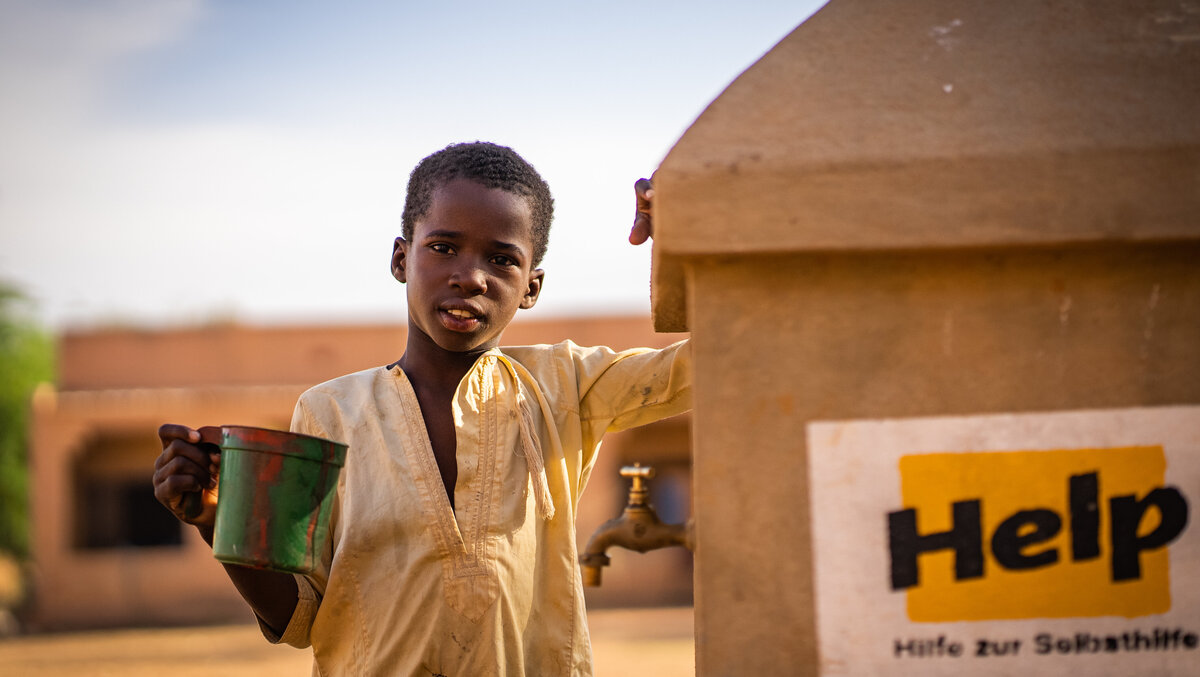 Ein Junge steht neben einem Help-Brunnen in Mali