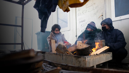 Drei Geflüchtete versuchen, sich an einem kleinen Feuer zu wärmen