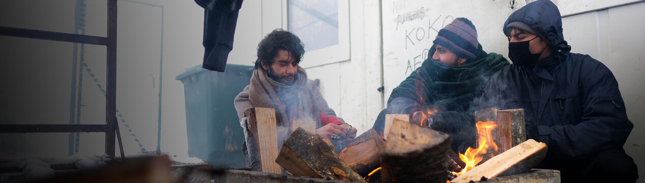 Drei Geflüchtete versuchen, sich an einem kleinen Feuer zu wärmen