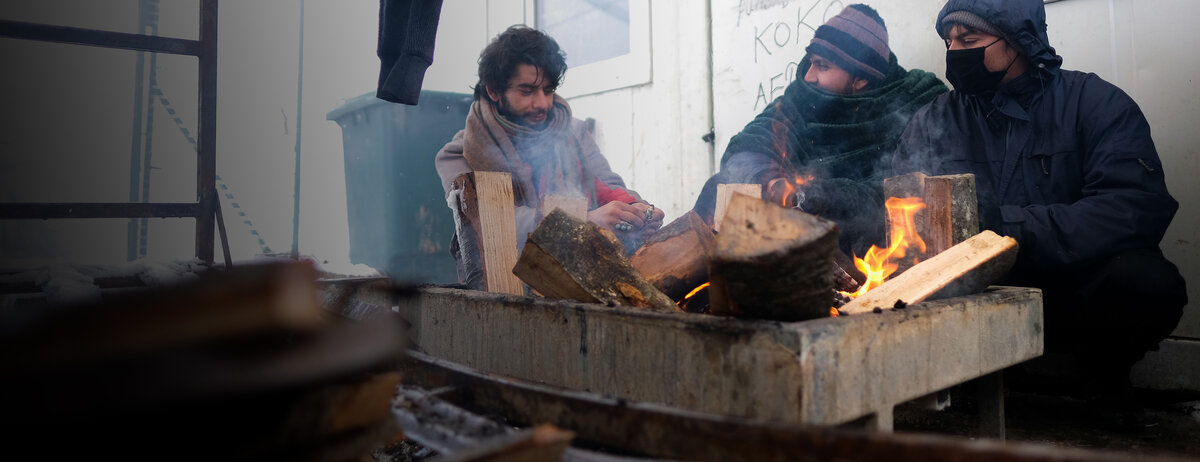Drei Geflüchtete versuchen, sich an einem kleinen Feuer zu wärmen