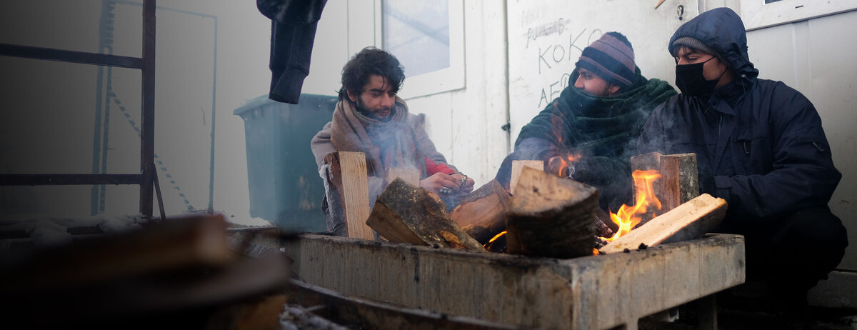Drei Geflüchtete versuchen, sich an einem kleinen Feuer zu wärmen