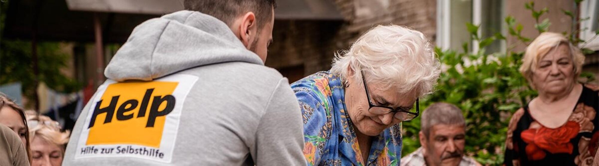 Ein Help-Mitarbeiter überreicht einer älteren Dame Hilfsgüter