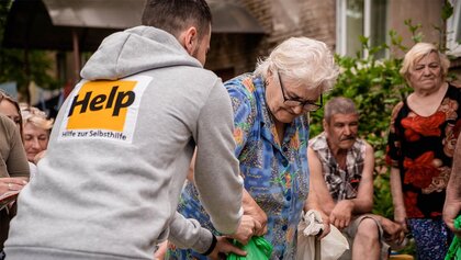 Ein Help-Mitarbeiter überreicht einer älteren Dame Hilfsgüter