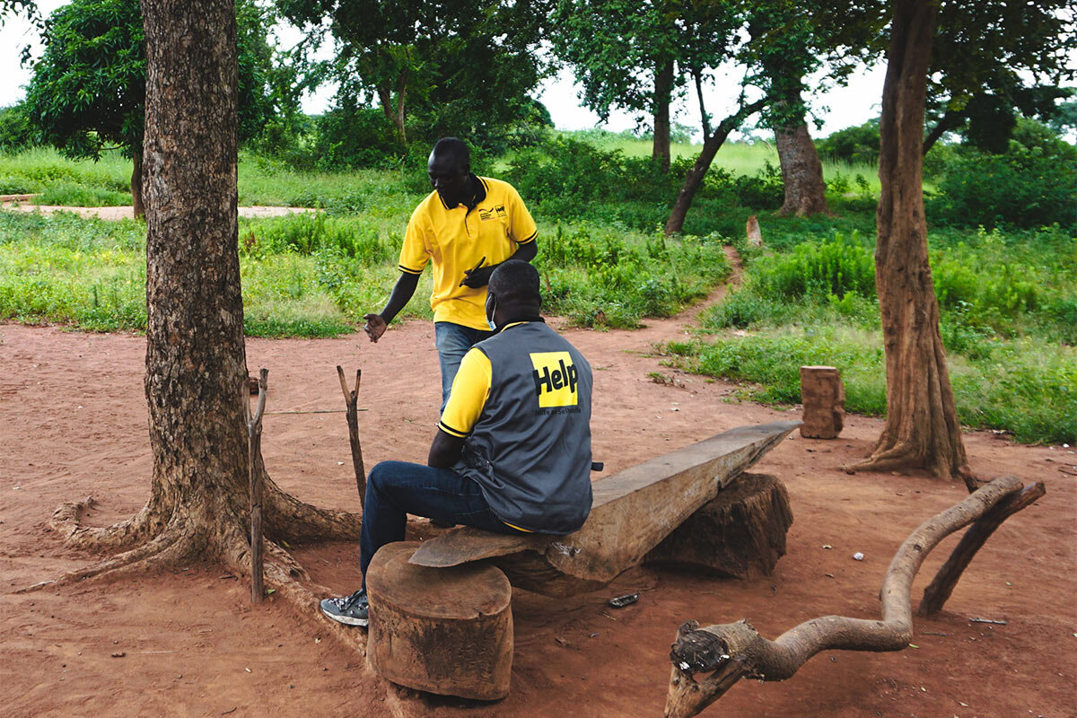 Help fördert Bildungsmaßnahmen im Südsudan, beispielsweise den Bau von Schulen Zwei Help-Mitarbeiter im Südsudan in einem typischen Klassenzimmer im Freien.