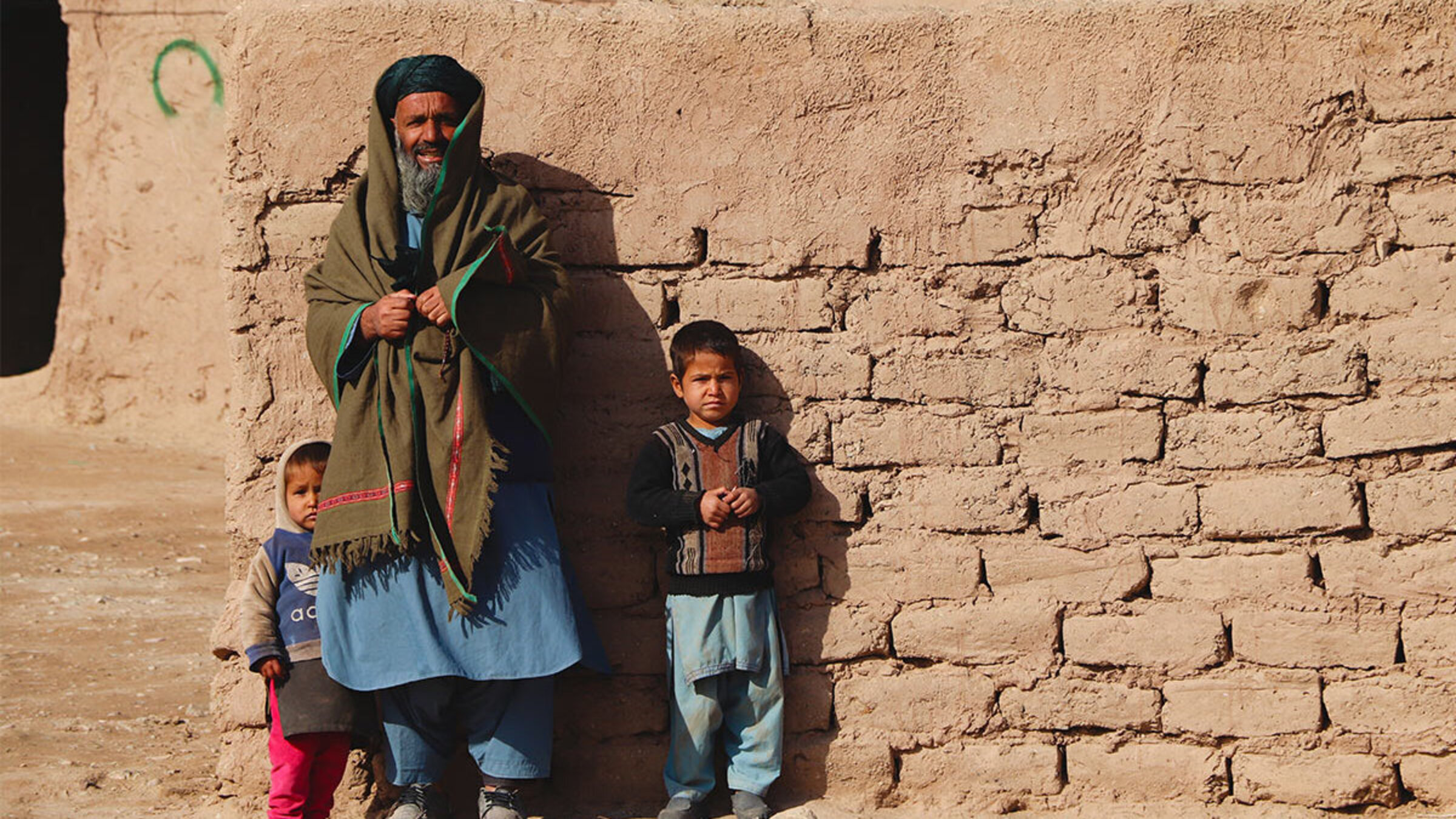 Ein afghanischer Vater und seine zwei Kinder stehen vor einer Mauer.