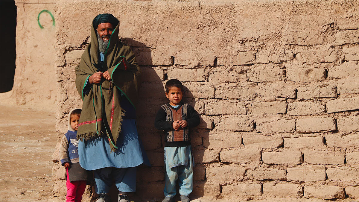 Ein afghanischer Vater und seine zwei Kinder stehen vor einer Mauer.