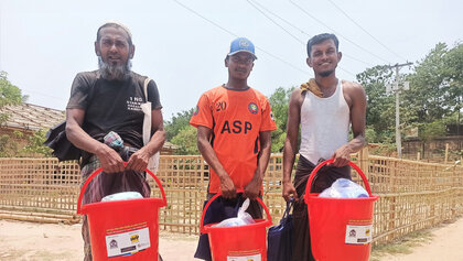 Drei Rohingya-Männer empfangen Hilfsgüter von Help