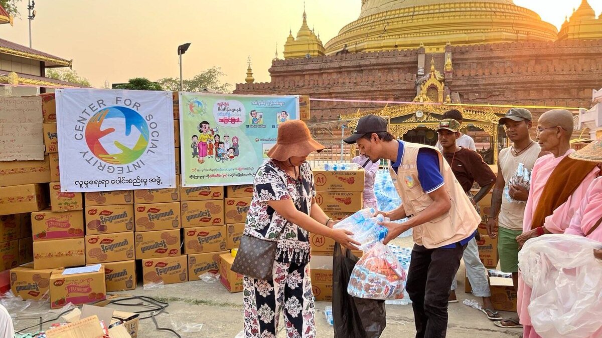 A humanitarian worker hands food and water to a woman